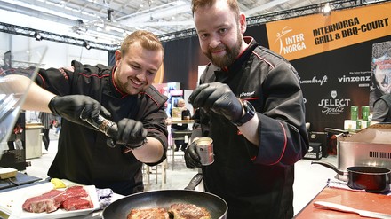 Zwei Köche würzen Fleisch in der Pfanne Zwei Köche würzen Fleisch in der Pfanne
