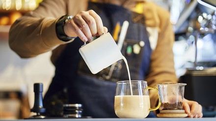 Thekenkraft gießt Milch in ein Glas Thekenkraft gießt Milch in ein Glas