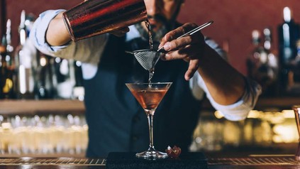 Barkeeper schüttet Cocktail über Sieb in ein Glas