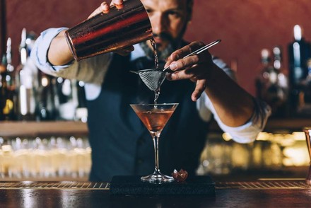 Barkeeper schüttet Cocktail über Sieb in ein Glas