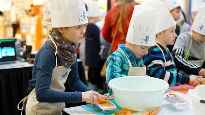 Kleine Kinder mit Kochmützen kochen zusammen an einem Tisch