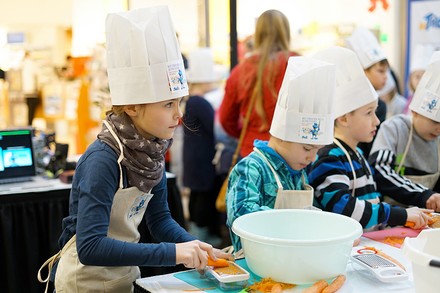 Kleine Kinder mit Kochmützen kochen zusammen an einem Tisch