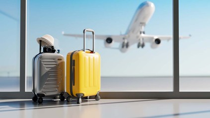 Koffer stehen am Flughafen, im Hintergrund startet ein Flurgzeug