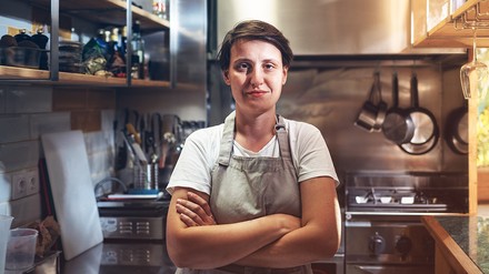 Junge Gastronomin steht mit verschränkten Armen in der Küche eines Restaurants