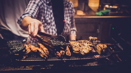 Mann an Grill hebt Fleisch mit Grillzange an