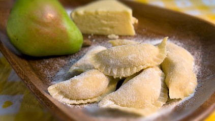 Mit Mehl bedeckte Ravioli, ein Stück Bergkäse und eine Birne auf einem Holzbrett