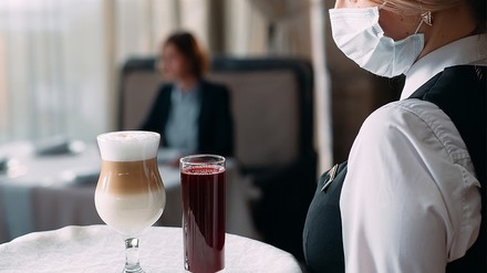 Bedienung im Restaurant mit Mund-Nasen-Schutz trägt ein Tablett mit Getränken