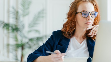 Junge Frau sitz vor einem Laptop und notiert sich etwas