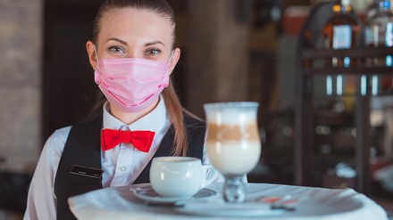 Junge Kellnerin mit Mund-Nasen-Maske und Getränketablett