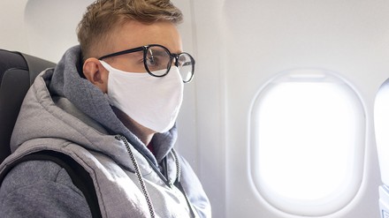 Junger Mann im Flugzeug trägt eine Mund-Nasen-Maske