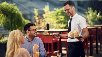 Glücklicher Kellner serviert das Essen für die Gäste