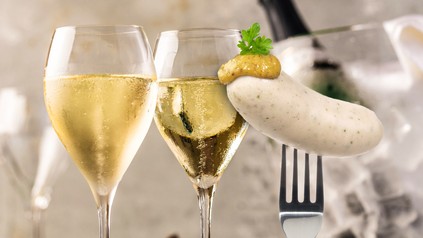 Zwei Gläser mit Champagner und eine Gabel mit Weißwurst