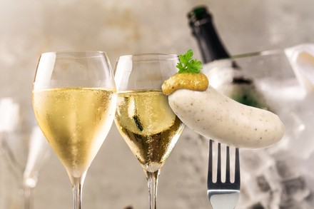 Zwei Gläser mit Champagner und eine Gabel mit Weißwurst