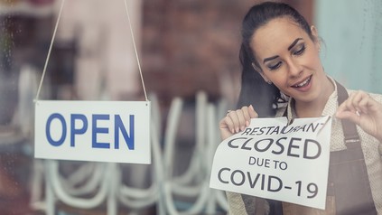 Gastronomin macht ein Closed Covid Schild ab, daneben hängt ein OPEN-Schild