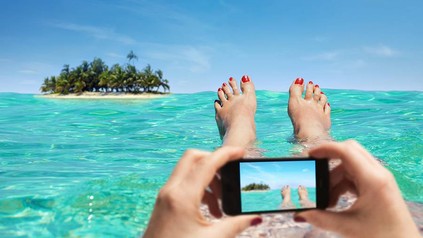 FRau liegt im Wasser und fotografiert eine Insel mit dem Handy