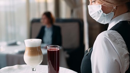 Kellnerin mit Mund-Nasen-Bedeckung bedient einen Gast im Restaurant