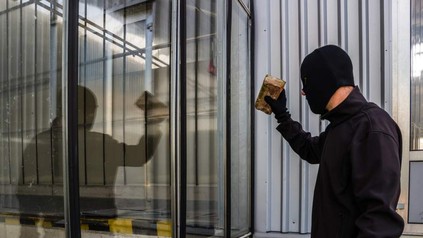 Einbrecher mit Ziegelstein vor Fenster