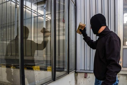 Einbrecher mit Ziegelstein vor Fenster