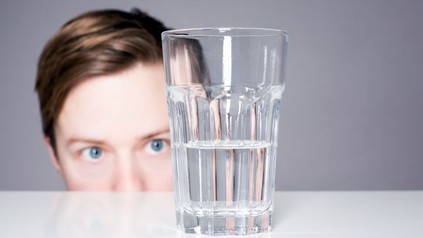 Mann schaut auf halb leeres Glas Wasser