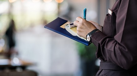 Kellner notiert etwas auf einen Block