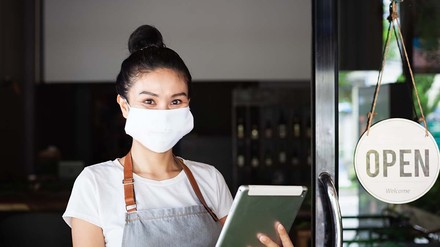 Junge Dame mit Maske kontrolliert Gäste beim Einlass in das Restaurant