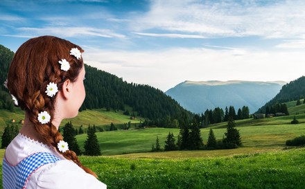 junge Frau im Dirndl schaut auf Alpenlandschaft