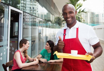Ein farbiger Kellner bedient zwei Gäste