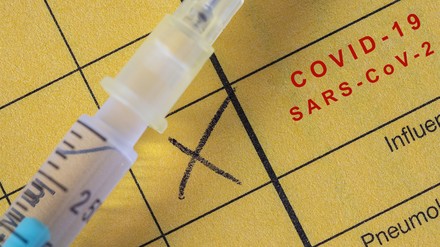 Impfbuch und Spritze mit Corona-Impfstoff