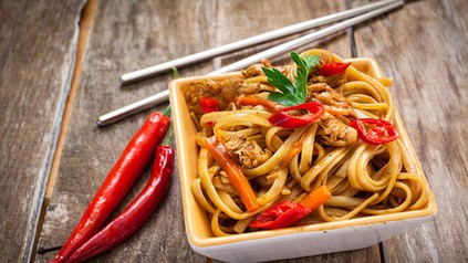 Eine Portion asiatische Chilinudeln mit Essstäbchen und zwei Chilischoten