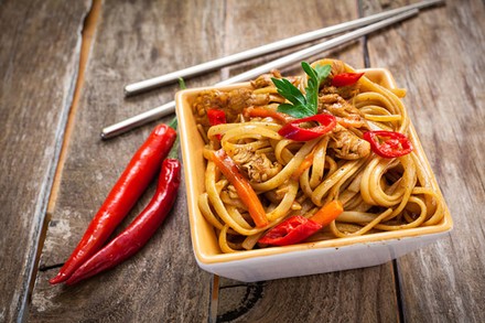 Eine Portion asiatische Chilinudeln mit Essstäbchen und zwei Chilischoten