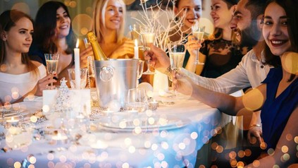 Eine Gruppe fröhlicher Menschen stößt mit Sekt gemeinsam an einem weihnachtlich gedeckten Tisch an