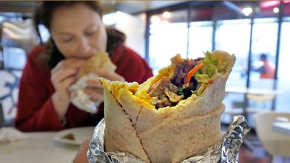 Ein Mann hält einen angebissenen Döner während eine Frau ihm gegenüber ebenfalls in einen Döner beißt