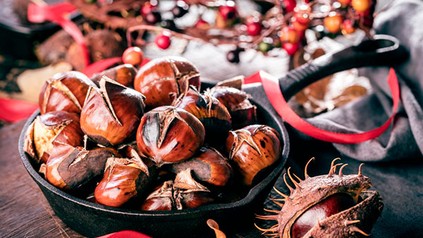 Frische Esskastanien in einer Pfanne, der Hintergrund ist weihnachtlich geschmückt