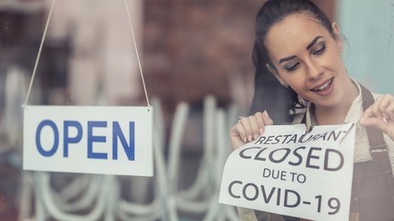 Gastronomin nimmt Closed-Schild ab und hängt OPEN an die Tür