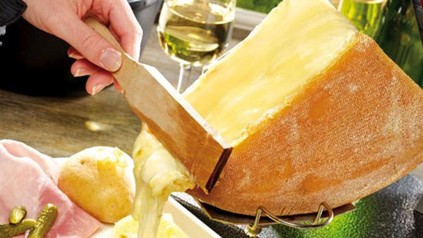 Eine Person schabt flüssigen Käse von einem großen Stück eines Käserads ab