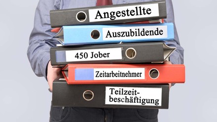 Mann hält Ordner mit der Aufschrift „Angestellte“, „Auszubildende“, „450 Euro Jober“ und „Teilzzeitbeschäftigte“