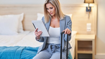 Junge Frau sitzt auf dem Hotelbett und checkt die digitale Gästemappe