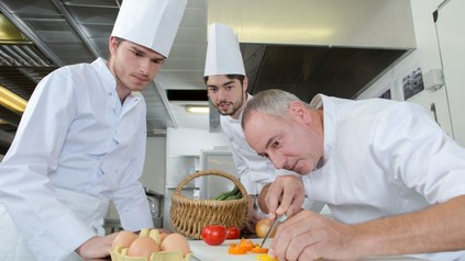 Ein Koch bringt seinen Auszubildenden etwas bei
