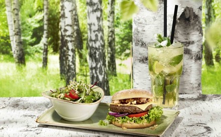 Eine Portion Burger und Salat mit einem frischen Getränk im Restaurant Hans im Glück. Im Hintergrund sieht man Birkenbäume