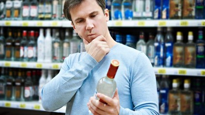 Ein Mann blickt nachdenklich auf eine Flasche Alkohol