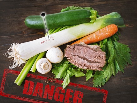 Ein Zucchini, ein Lauch in dem eine Nadel steckt, Pilze, eine Karotte und ein Stück Fleisch auf Kräutern, darunter ein Stempel auf dem Danger steht
