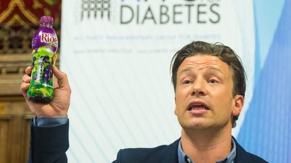 Jamie Oliver hält ein zuckerhaltiges Getränk in der Hand