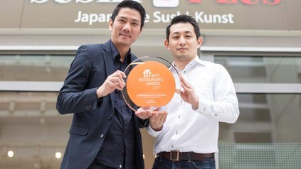 Zwei Asiaten stehen vor dem Sushi Plus Restaurant und halten den Preis für Best Restaurants Awards 2017 hoch