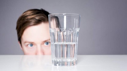 Eine Person starrt auf ein zur Hälfte gefülltes Glas Wasser