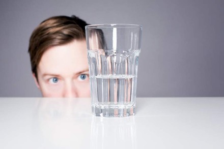 Eine Person starrt auf ein zur Hälfte gefülltes Glas Wasser