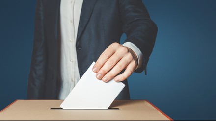 Mann im Anzug wirft Wahlzettel in Urne