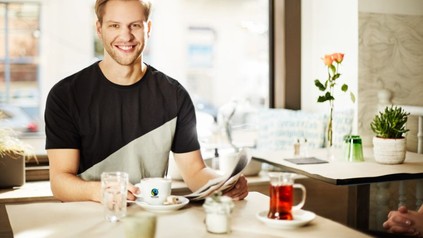 Ein junger Mann greift in einem Café eine Tasse Fairtradekaffee