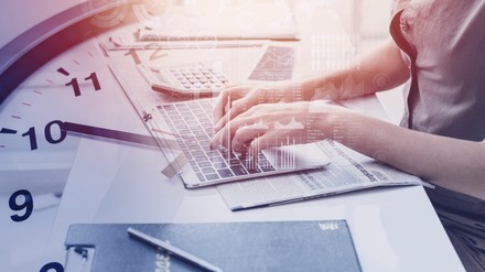 Frau an Laptop mit großer Uhr unterlegt