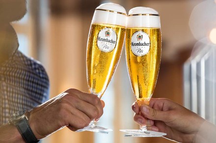 Zwei Personen stoßen mit Krombacher Pils in dazu passenden Gläsern an