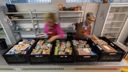 Zwei Tafelmitarbeiter sind mit dem Ausräumen von Supermarktkisten mit Lebensmitteln beschäftigt